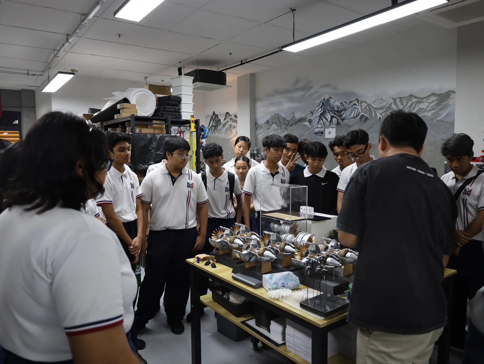 A secondary school group gathered round a workbench of 3D printed jet engine models in our studio while one of our trainers walks them through how the parts were printed