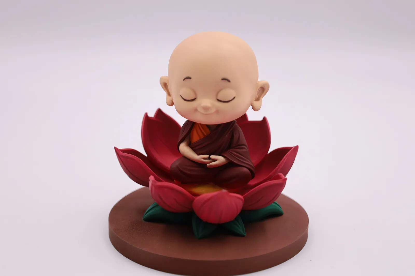 The finished monk figure painted in skin tone and a maroon robe, sitting on a red lotus on a brown base