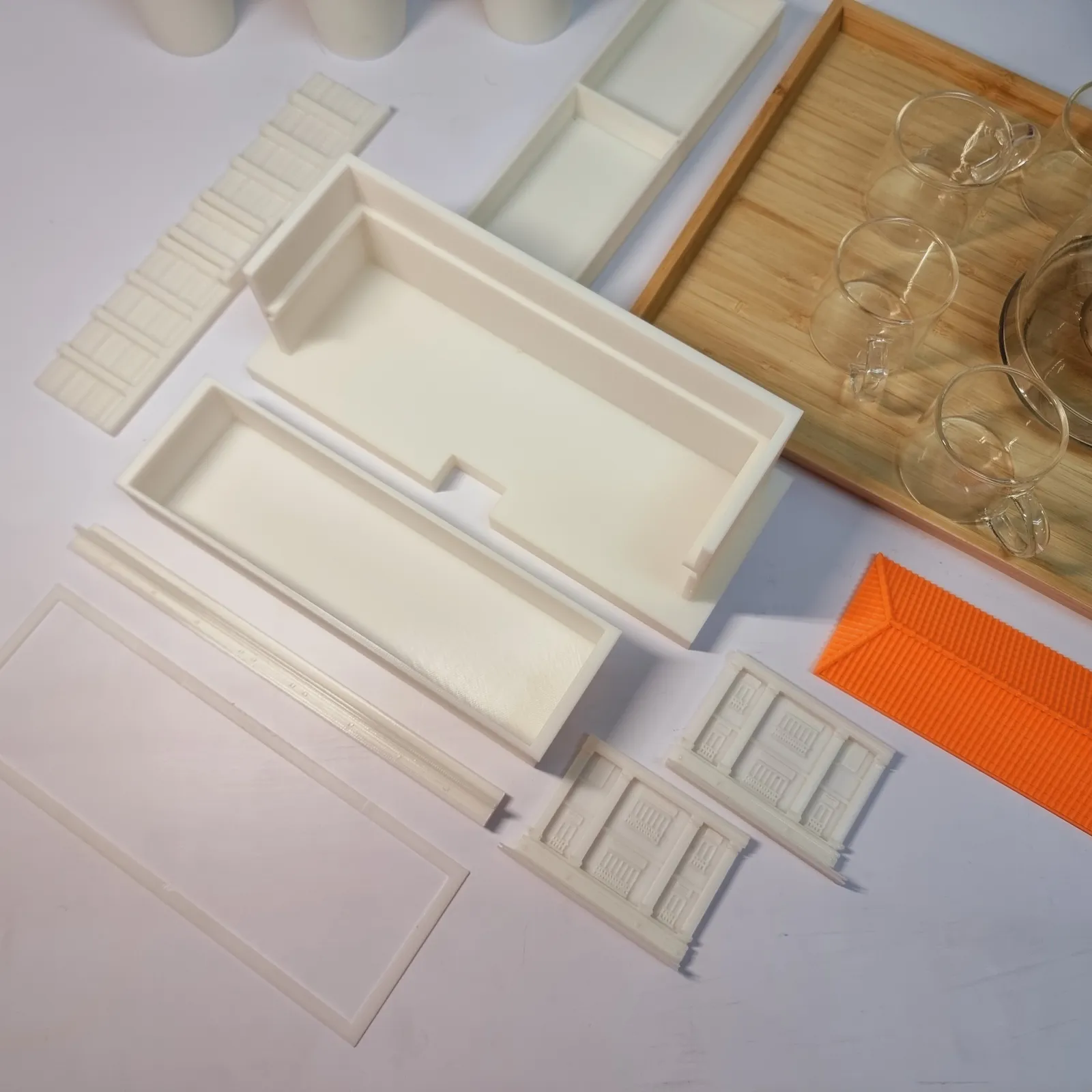 The printed parts of one of our building models laid out separately on a table before assembly, walls, facade panels, base frame and an orange roof