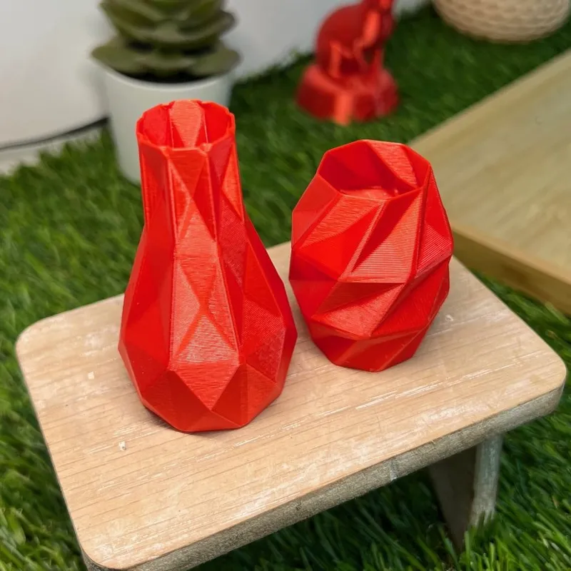 Two red faceted vases we 3D printed in PLA Basic, standing on a small wooden stool, their faces catching a light sheen