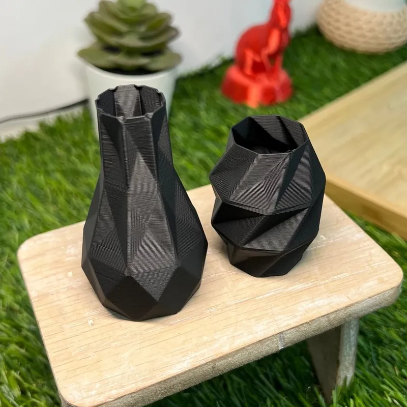 Two black faceted vases we 3D printed in PLA Matte, standing on a small wooden stool, with no shine on their faces