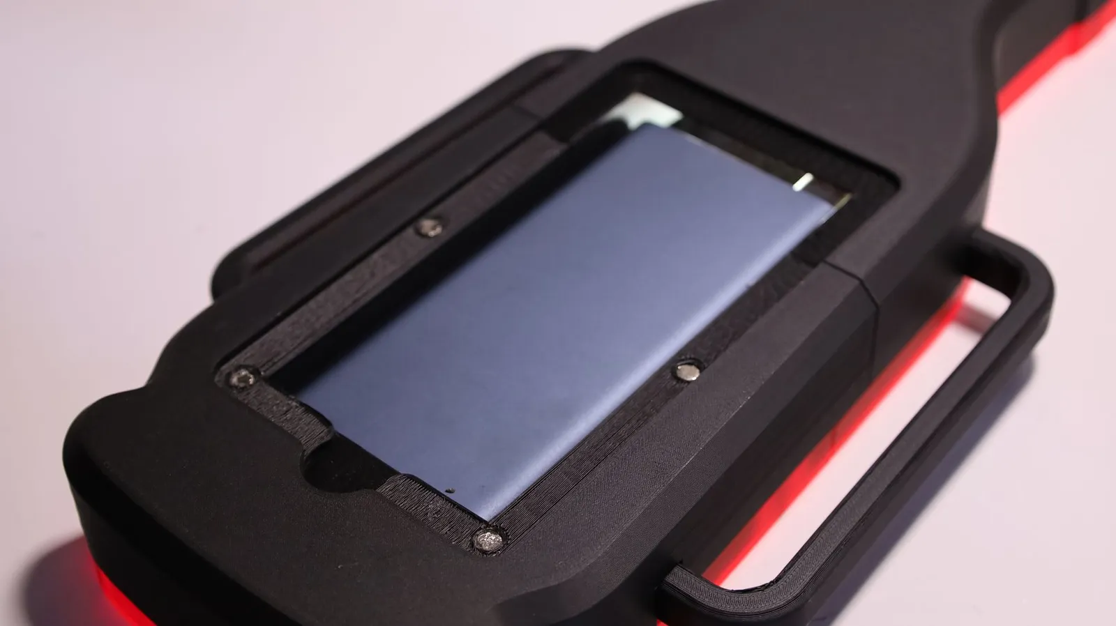 The back of the black 3D printed Hennessy maze, a compartment in the print holding the battery pack under a screwed frame, with red LED light glowing at the edges
