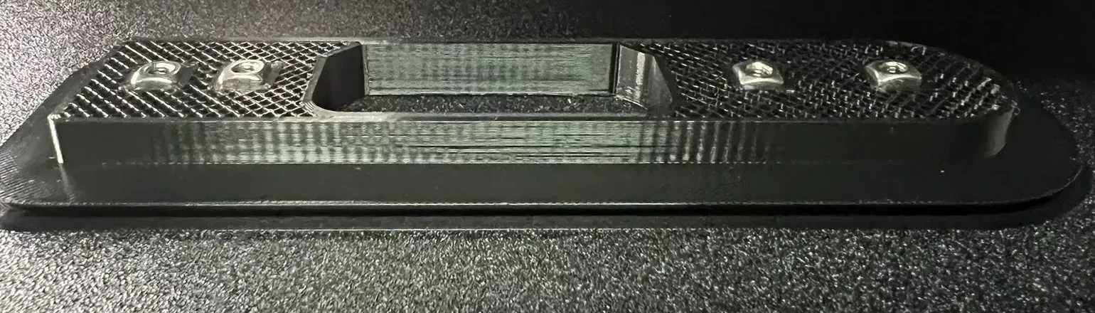 Four square nuts sitting in their pockets in a black 3D print, paused mid-print on the printer bed with the infill still open