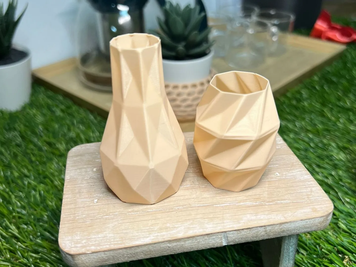 Two faceted beige PLA vases on a small wooden stool, with faint layer lines across each face