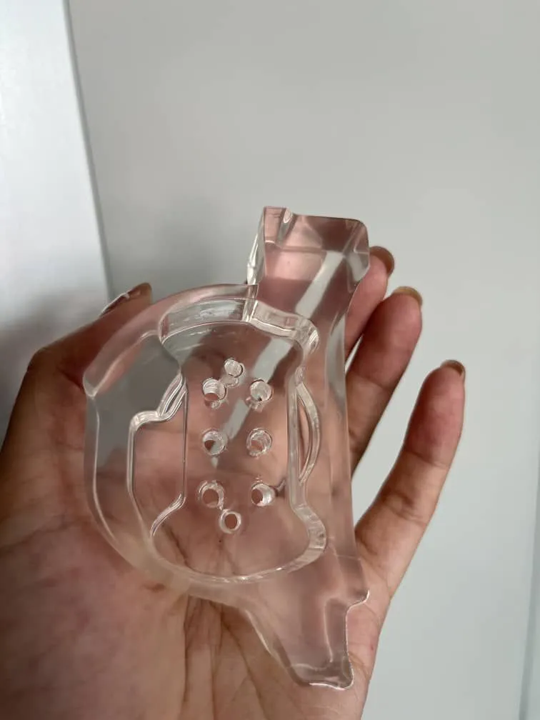 A clear resin printed part held in a hand, smooth all over, with a row of small holes through its base