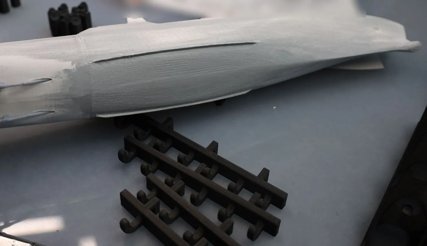 The printed hull of a frigate model on the bench, grey filler brushed over its layer lines, with a brush and printed parts beside it