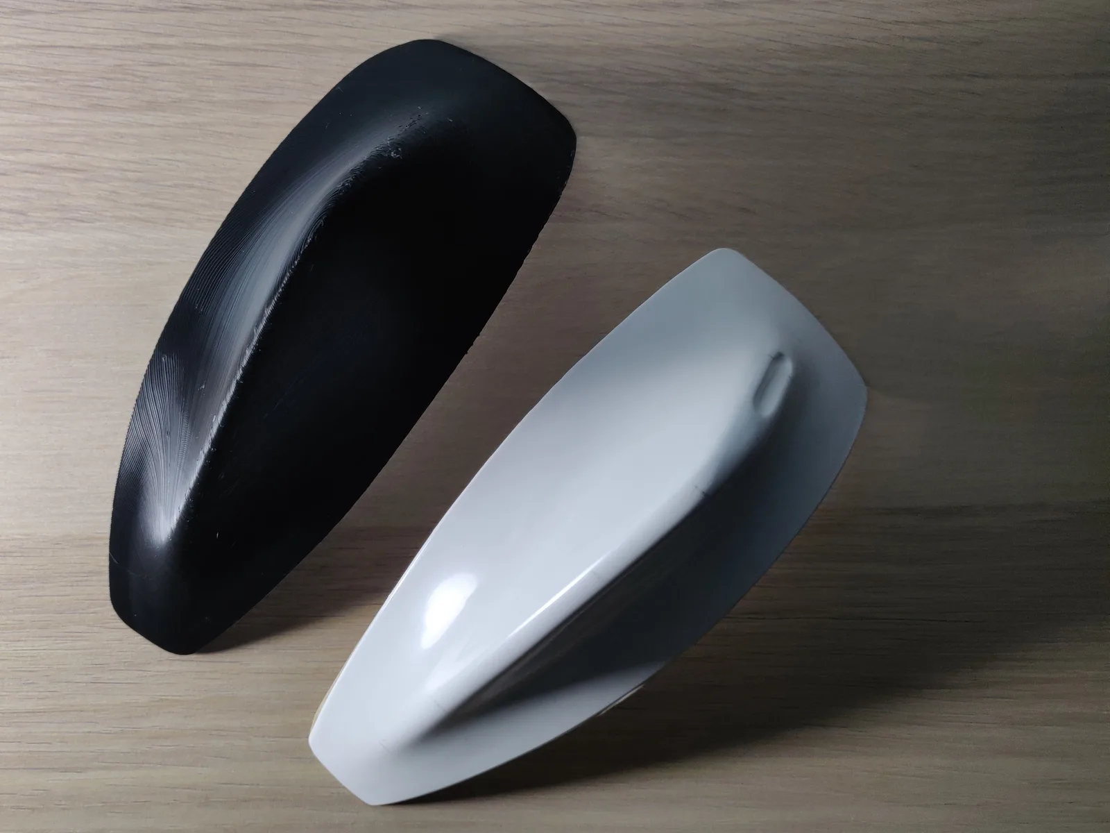Two copies of the same curved helmet fin: on the left a raw black 3D print with fine layer lines across its surface, on the right the same shape filled, sanded and finished in smooth glossy white