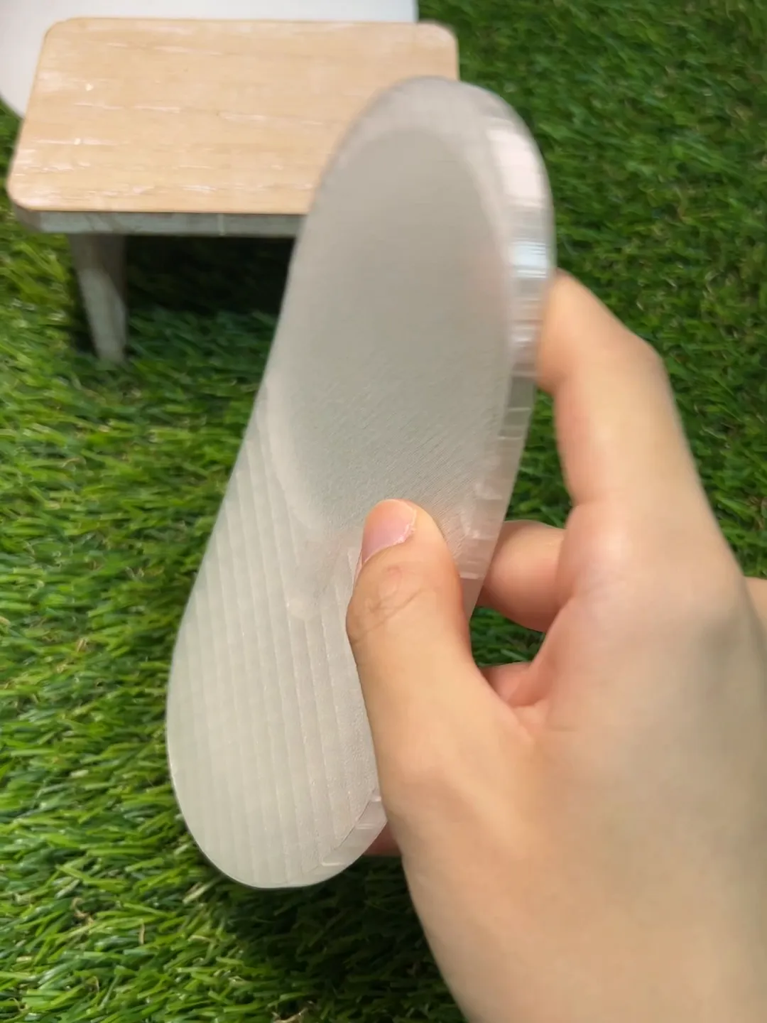 A hand bending a frosted, see-through 3D printed TPU part into a curve, with the fine printed lines visible across its surface