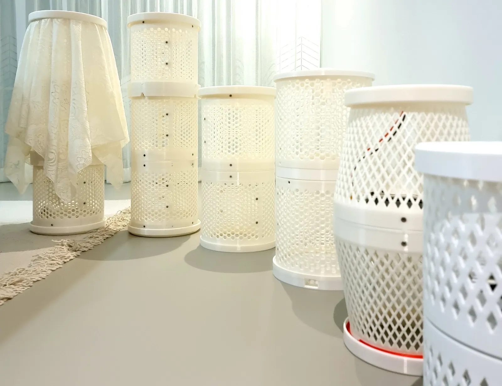 Six white 3D printed air purifier prototypes standing in a row, from early round housings with hexagon vents to the final hourglass shape with a diamond lattice