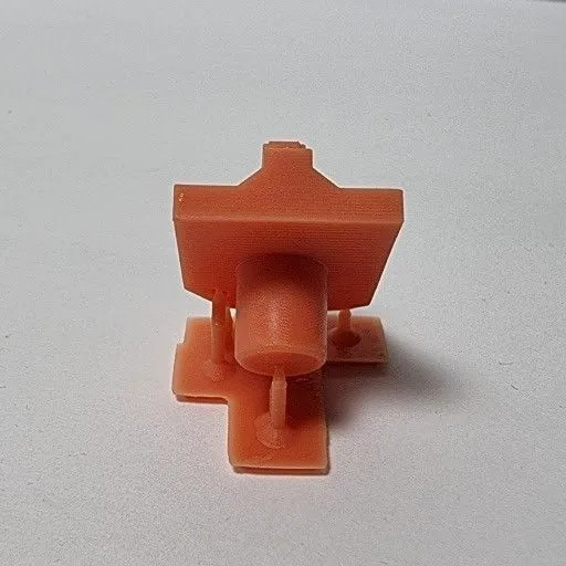 An orange filament printed part still standing on thin printed support pillars, before they are snapped off
