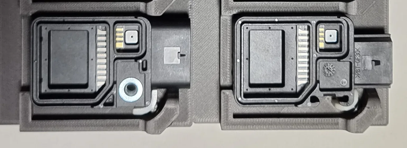 Top-down view of two black connectors each seated flat in its own pocket in a grey printed holding tray, with an even gap showing all round