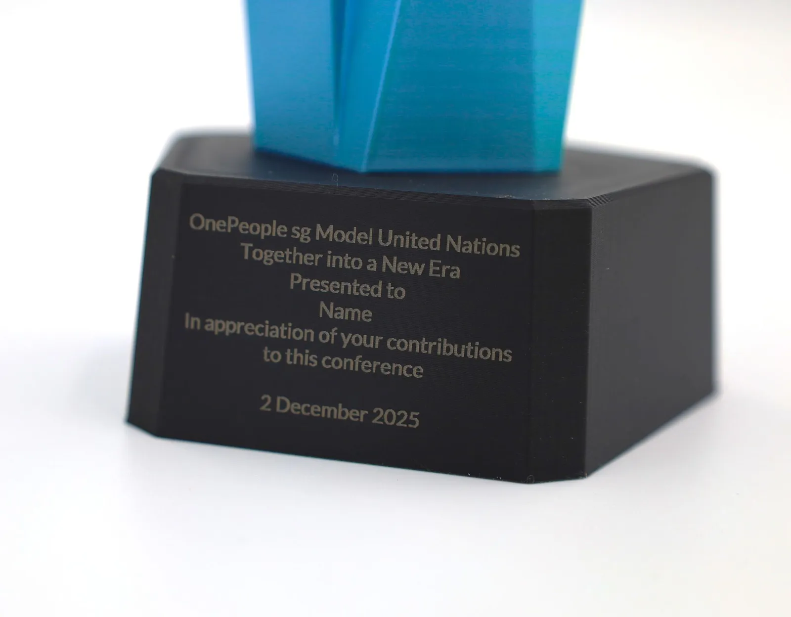 Lines of text laser engraved into the matte black 3D printed base of a blue trophy
