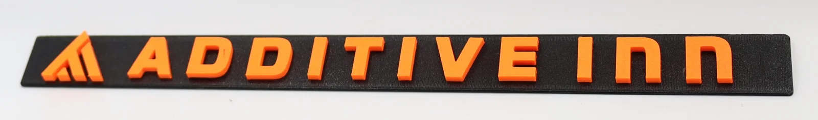 The ADDITIVE inn logo and lettering printed raised in orange on a long black 3D-printed bar