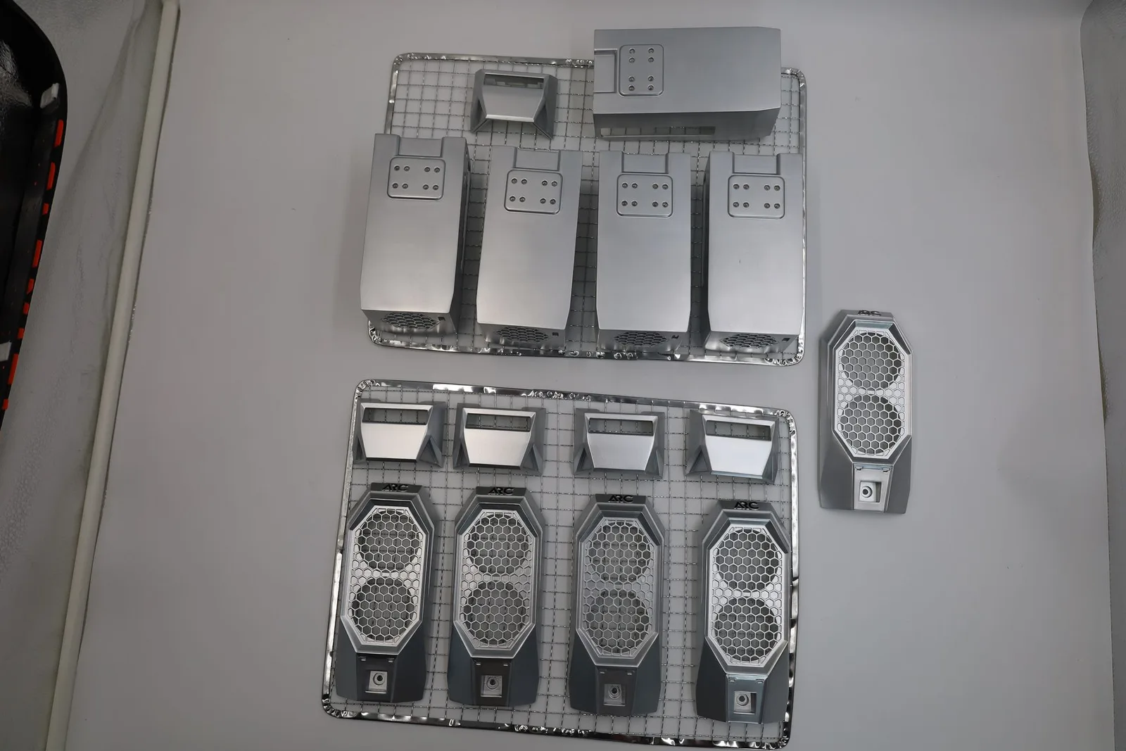 Two wire racks holding nylon computer case parts sprayed silver: long side shells, front grilles with honeycomb openings and small trims