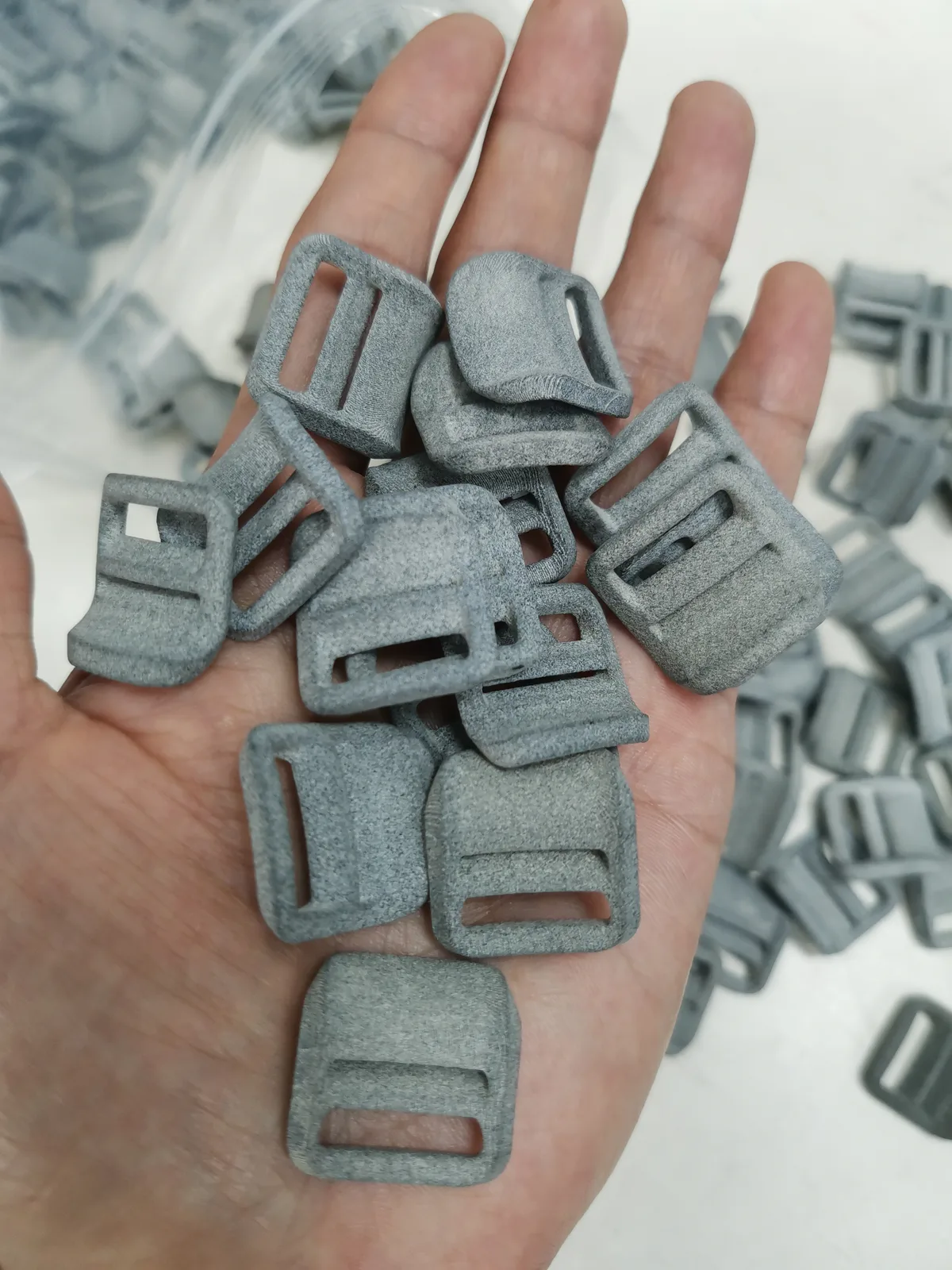 A handful of grey nylon strap buckles, their matte surface visibly grainy, from a batch printed in nylon powder