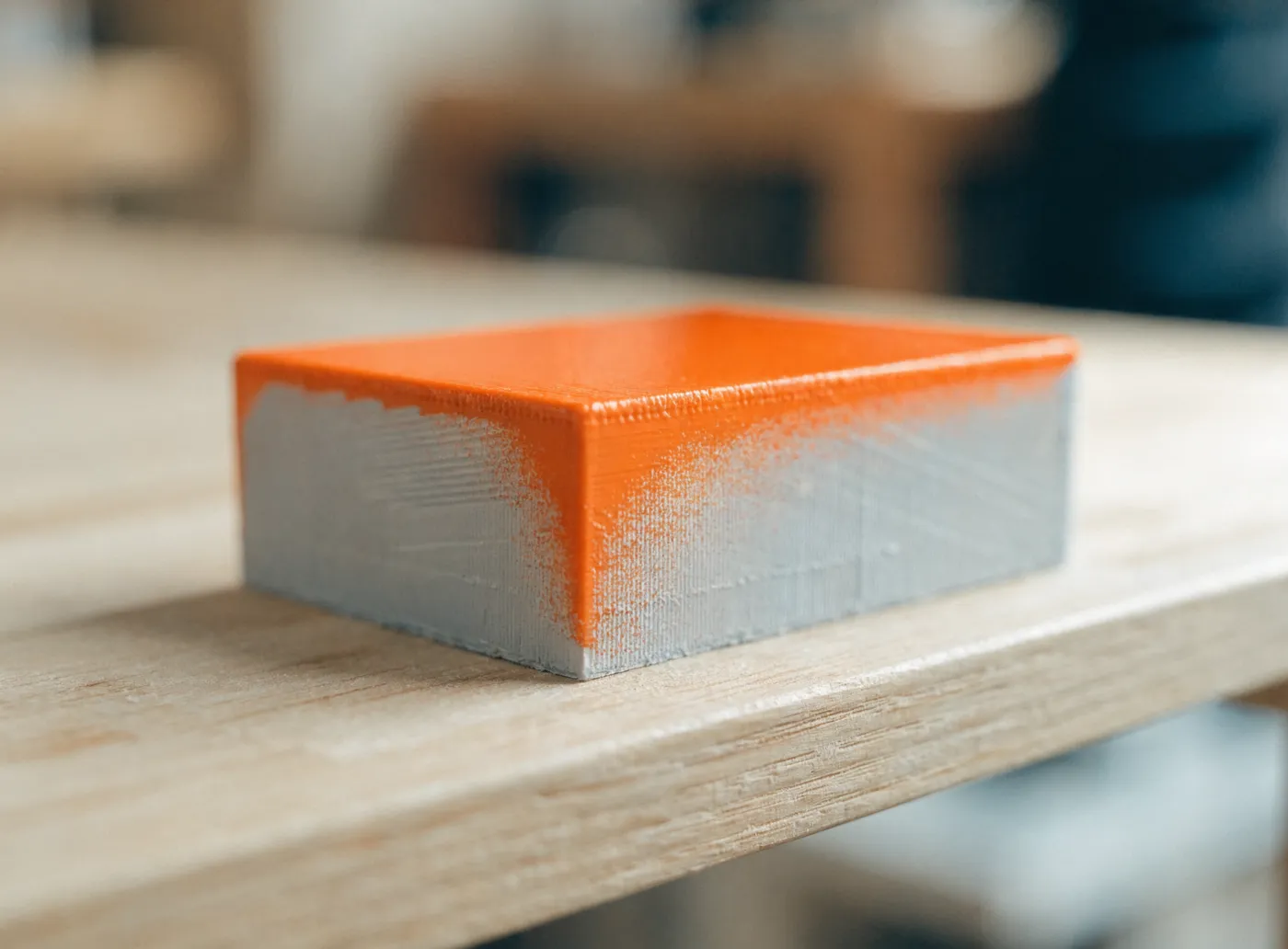 A 3D-printed part with a painted top and orange overspray fading down its raw grey side