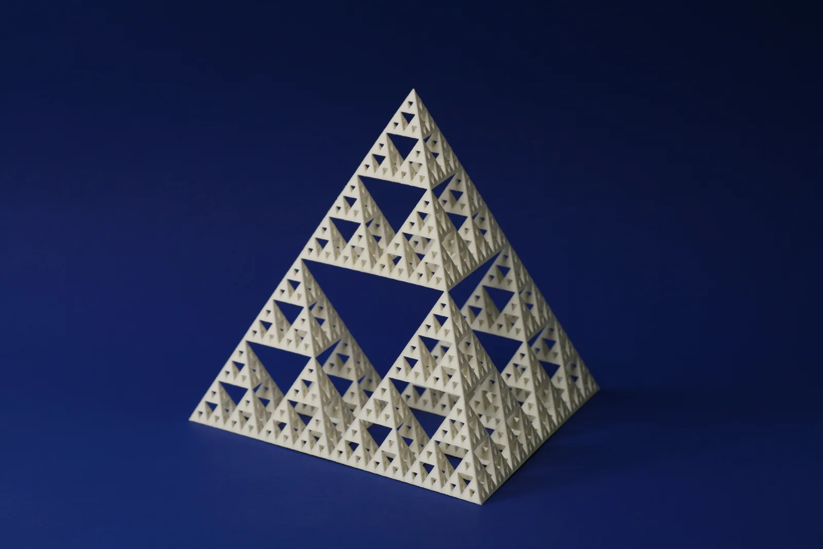 A cream-coloured nylon lattice shaped as a Sierpinski tetrahedron, printed by selective laser sintering, on a blue background