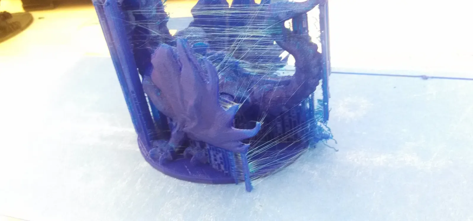 A blue printed dragon with fine strands of plastic stretched between its wings and body