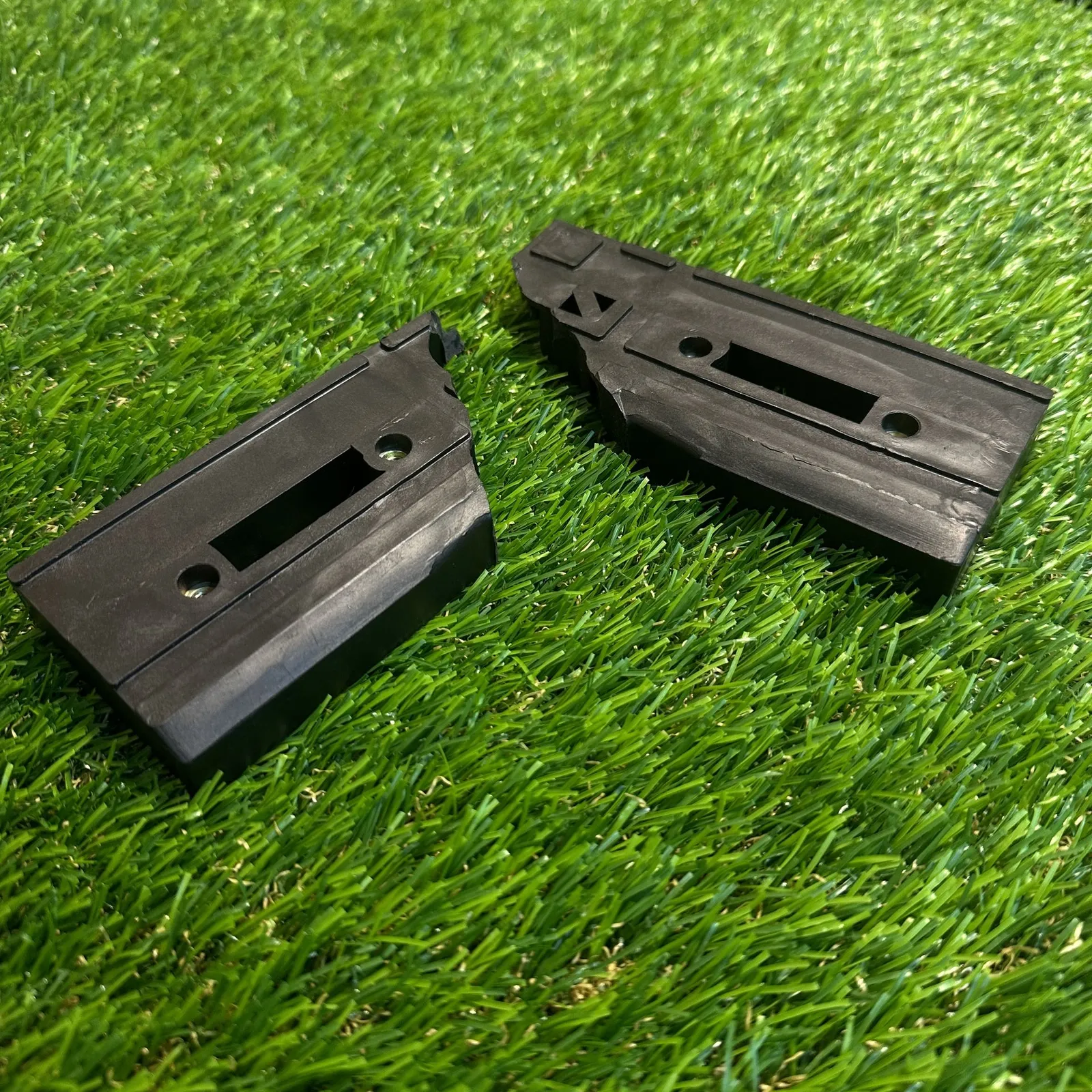 Two pieces of a snapped black plastic projector bracket lying on artificial grass