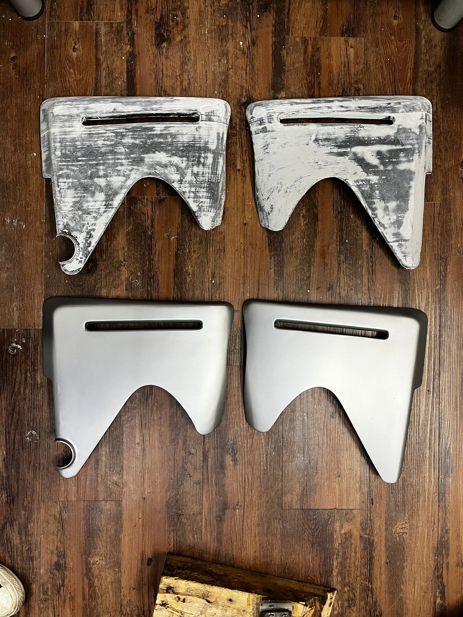 Two sun-faded, scratched original motorbike side panels at the top of a wooden floor, with two new smooth grey panels of the same shape below them