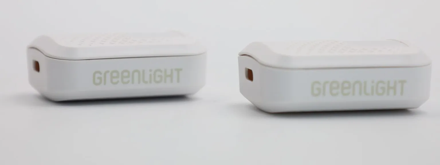 Two white GPS tracker casings side by side, each with the GREENLIGHT logo silk screen printed in light green along its side