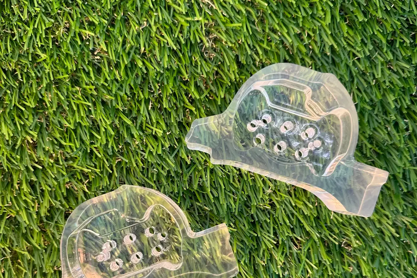 Two clear resin domes lying on grass, the blades of grass clearly visible through the parts