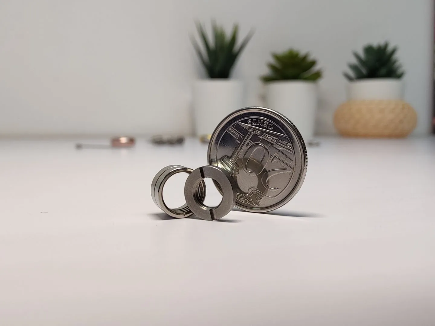Two small machined metal rings standing on a white table beside a Singapore 20-cent coin, both smaller than the coin