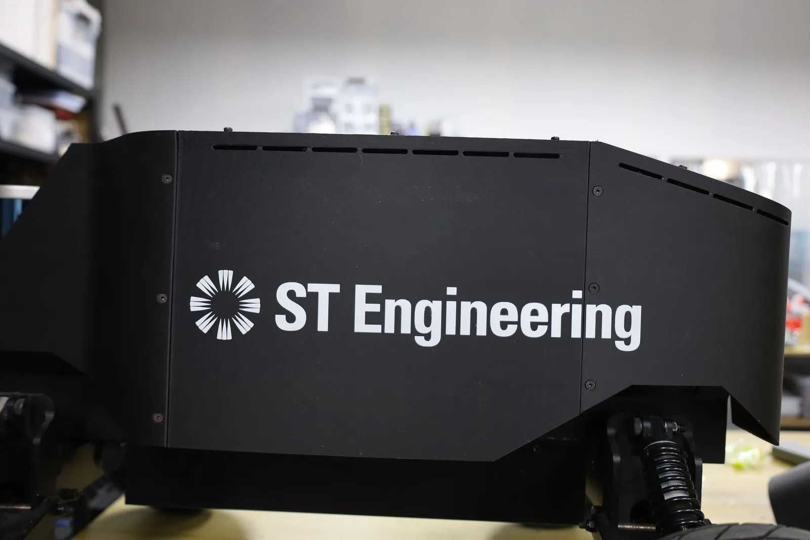 A black carbon-fibre PETG 3D printed robot casing with the ST Engineering logo UV printed in white across its flat side panel