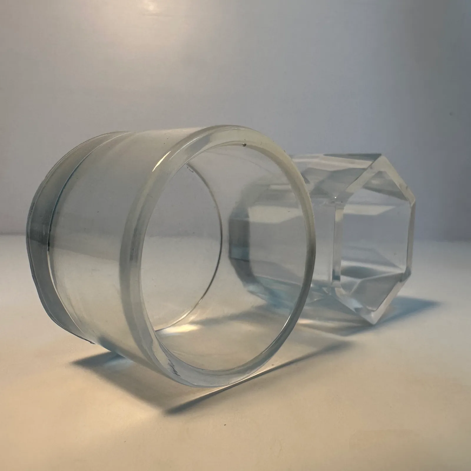 A clear cast resin cup lying on its side, round at the open end and with an eight-sided faceted base, both see-through