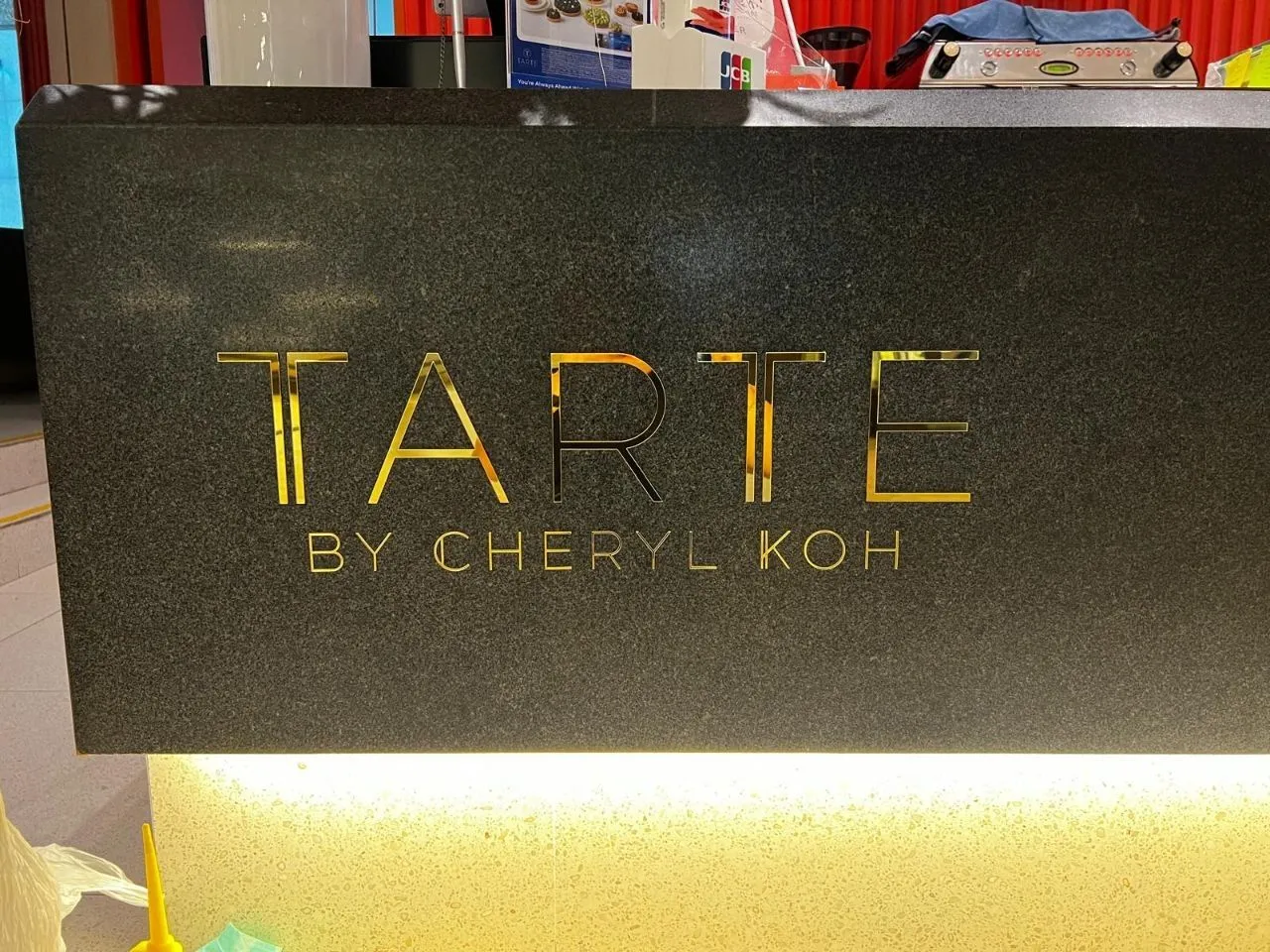 The words Tarte by Cheryl Koh in mirror gold acrylic letters on the dark granite front of a shop counter