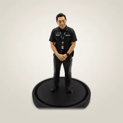 A hand-painted figurine of a man in a black polo shirt and lanyard, on a black base