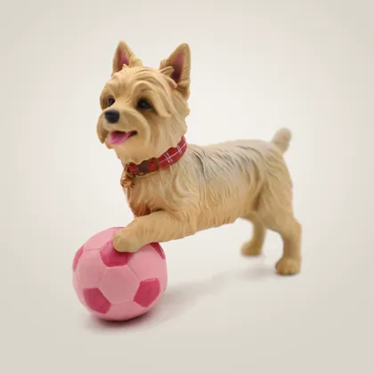 A hand-painted terrier figurine with a tartan collar, one paw on a pink football