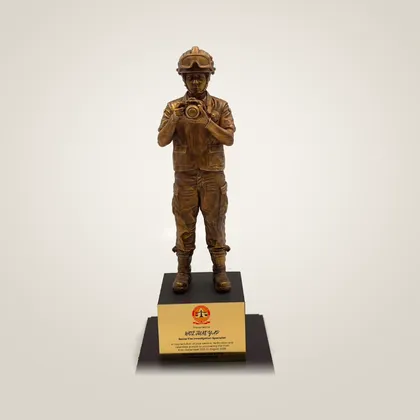 A bronze-finished figurine of a fire investigator with a camera, on an engraved plinth