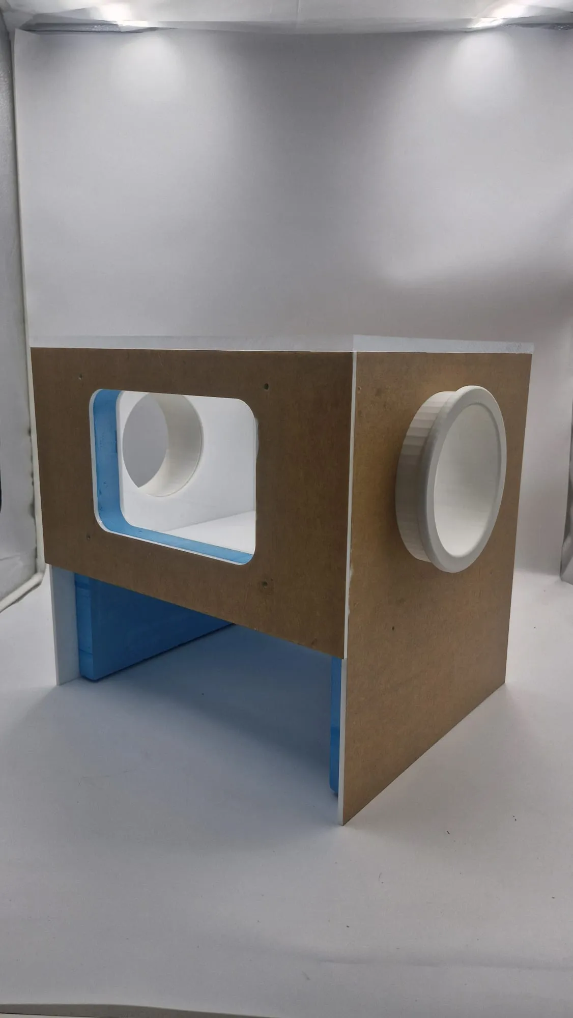 The finished glove box from a front corner: a viewing window framed in blue foam on one face and a white glove port on the other, raised on its stand