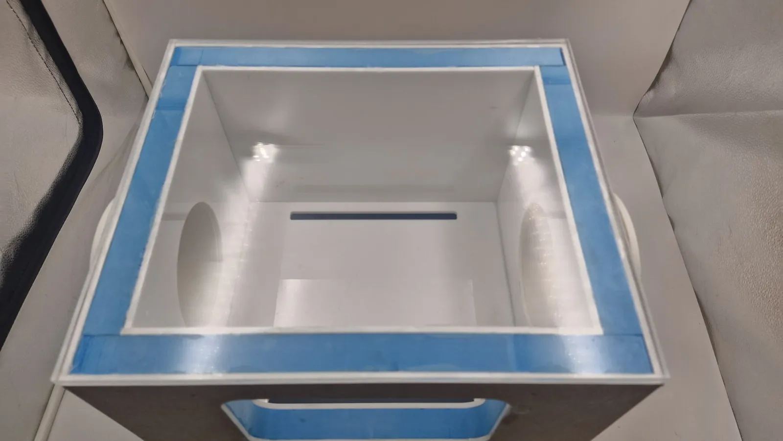 Looking down into the open box: white acrylic walls, the two round glove ports facing each other and the blue foam rim around the top