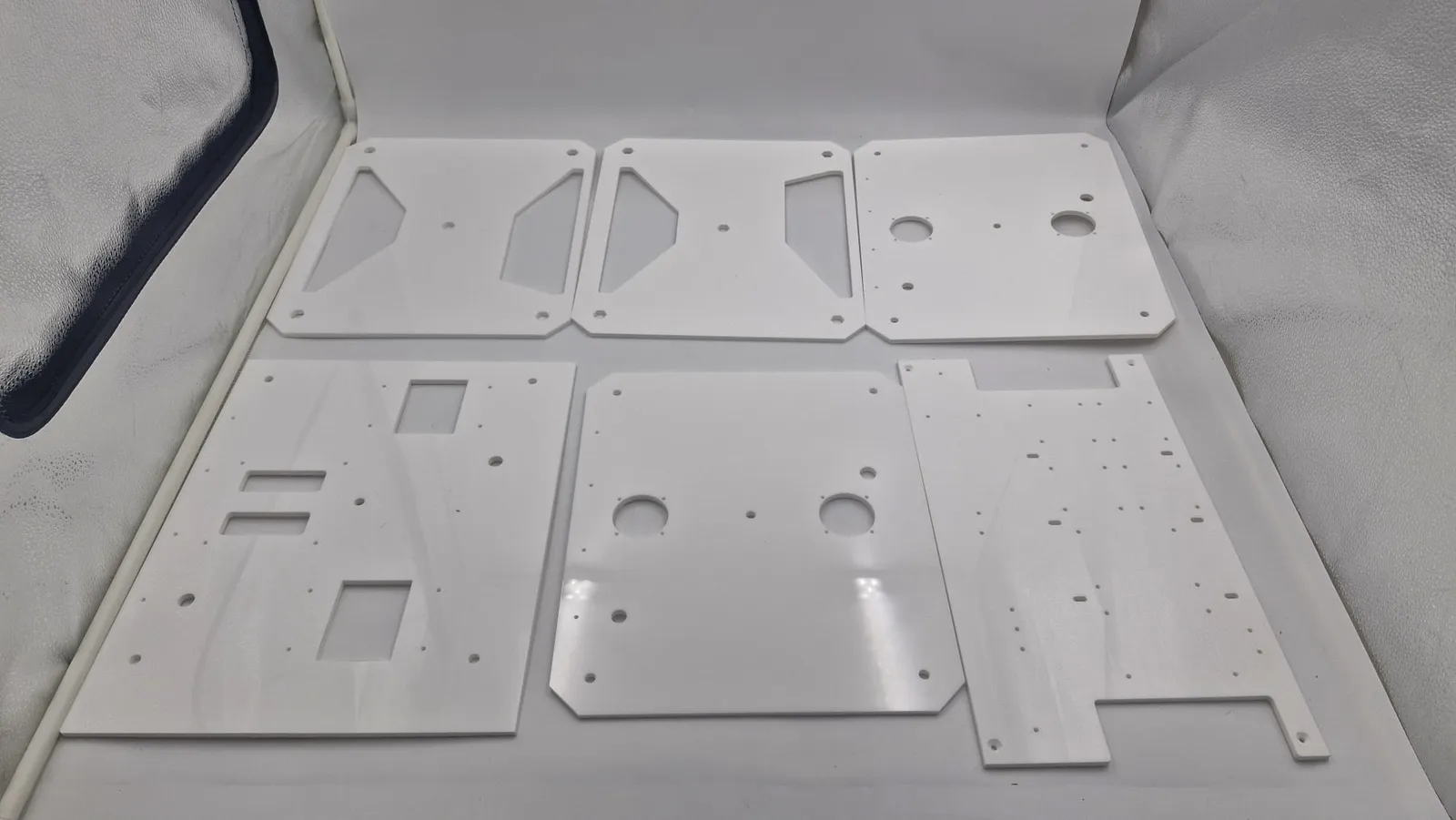 Six white laser-cut acrylic plates laid flat, with rectangular and round cut-outs and rows of drilled holes for fixings