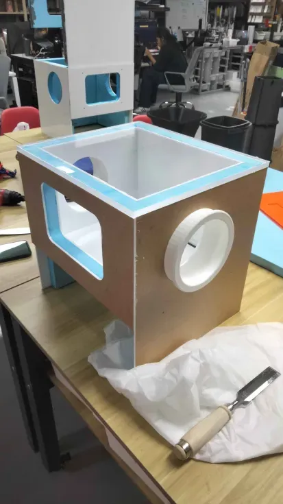 The assembled box on the workbench, with its viewing window, a white glove port and the blue foam rim around the open top