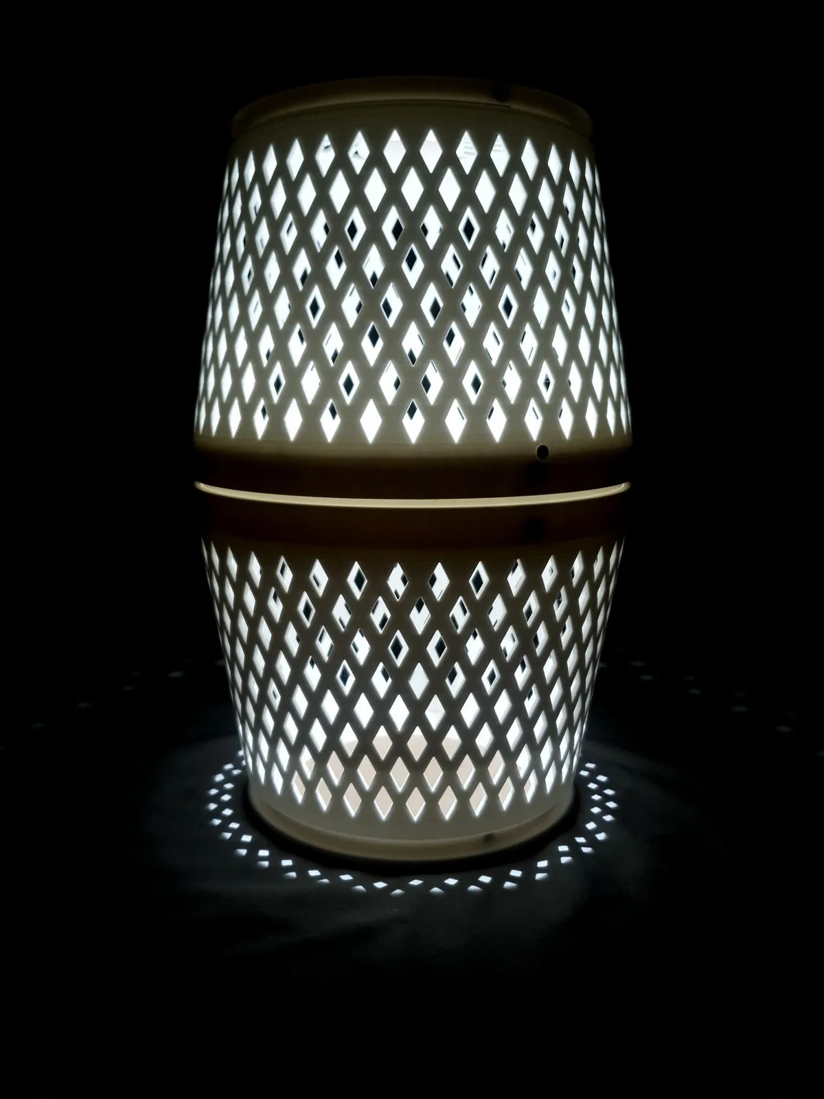 The white purifier lamp lit against a black background, light pouring through the diamond lattice and a ring of light on the floor below