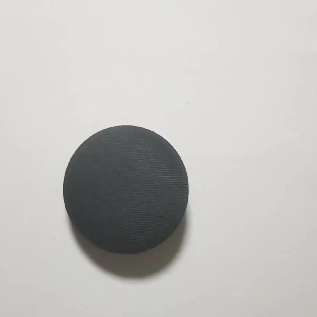 A charcoal Google Nest Mini smart speaker lying flat on a white surface, before its stand was made
