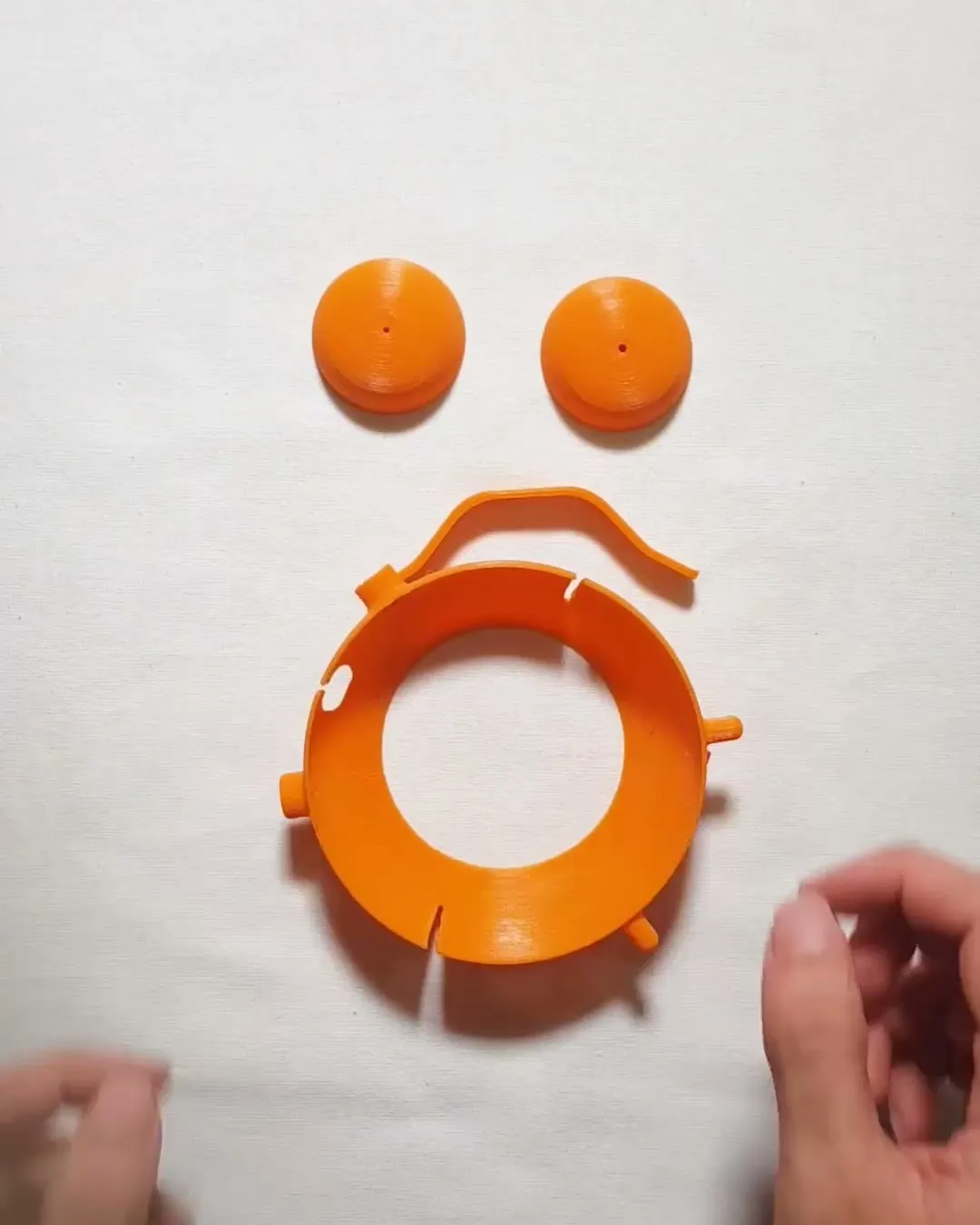 The four orange printed parts laid out on a white surface: two bells, the curved handle and the ring with its feet