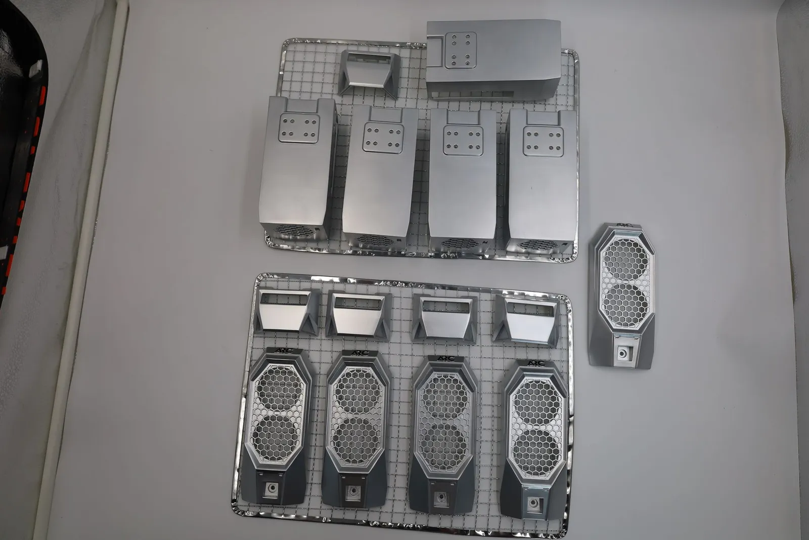 Arc case parts, sprayed silver, on two wire racks and the table: front panels with honeycomb grilles, top caps, rear panels
