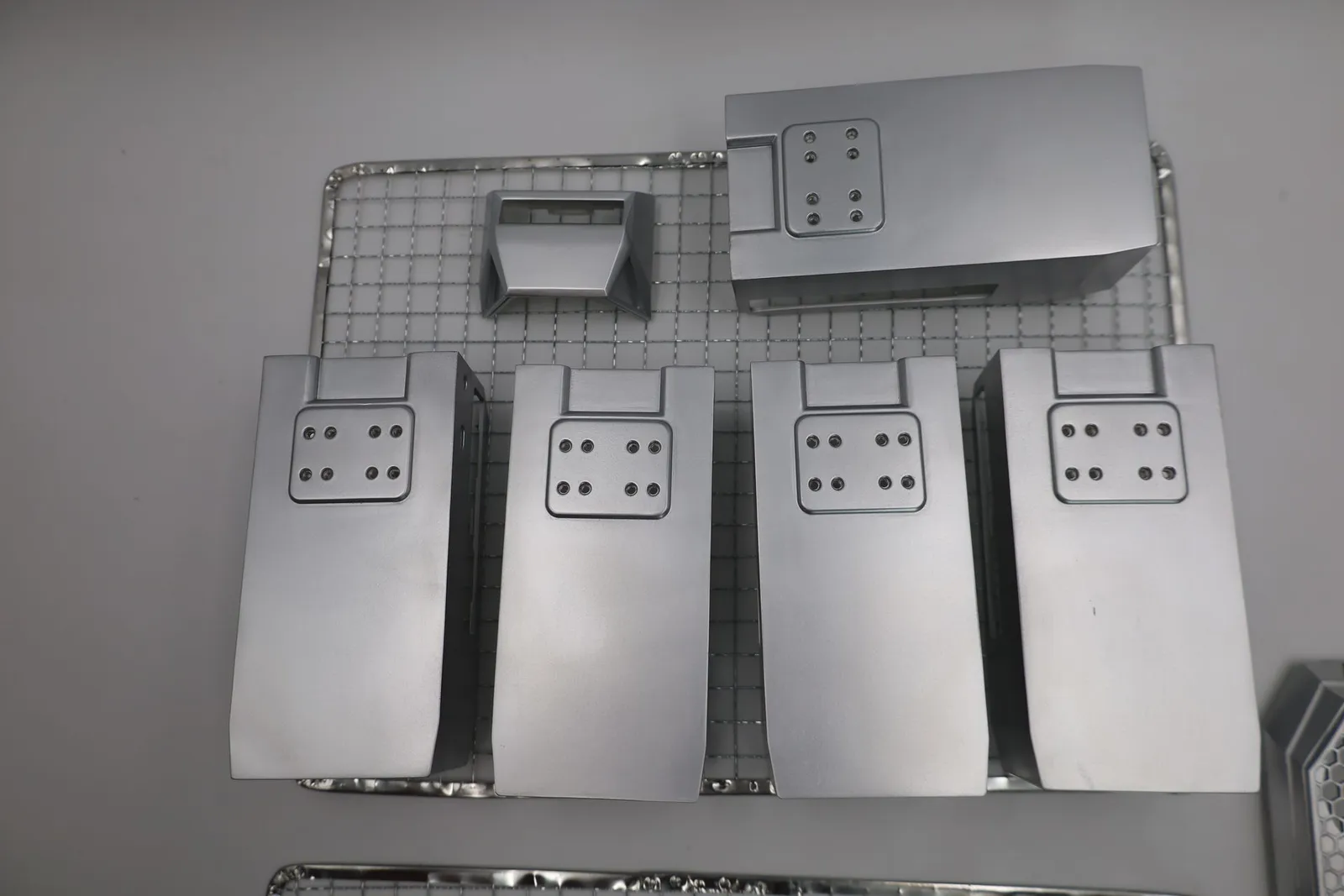 Four silver-sprayed rear panels, a top cap and a larger shell on a wire rack, each rear panel with a recessed pad of eight