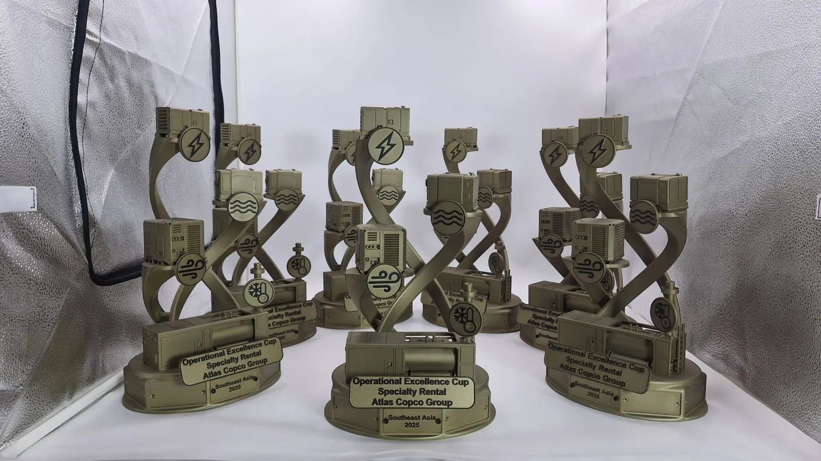 Part of the finished set in a light tent: gold trophies, each with miniature machines, icon discs and a black-lettered plate