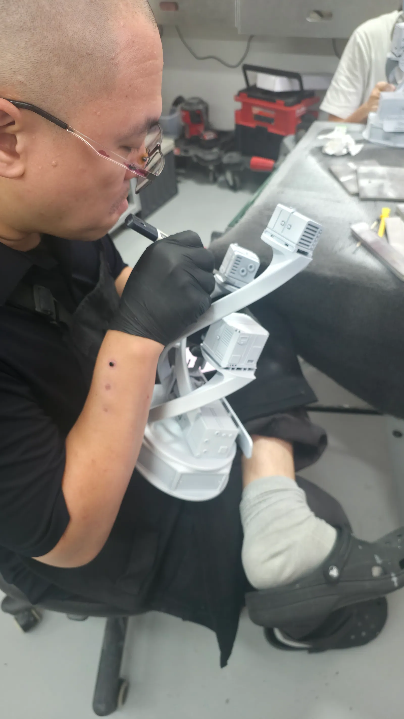 A finisher in black gloves working on a primed grey trophy held on his lap