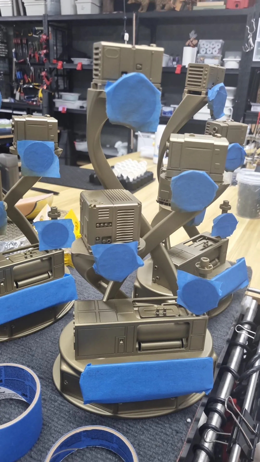 Gold trophies on a workbench with the icon discs and plates covered in blue masking tape