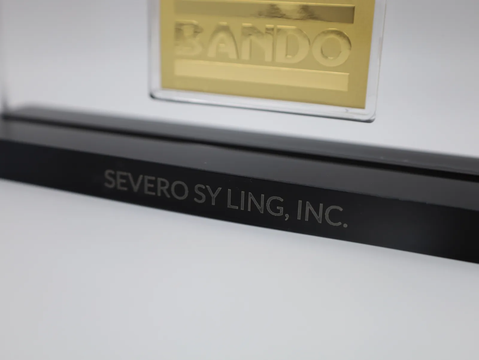 The black base engraved with the recipient's name, SEVERO SY LING, INC., below the gold BANDO bar