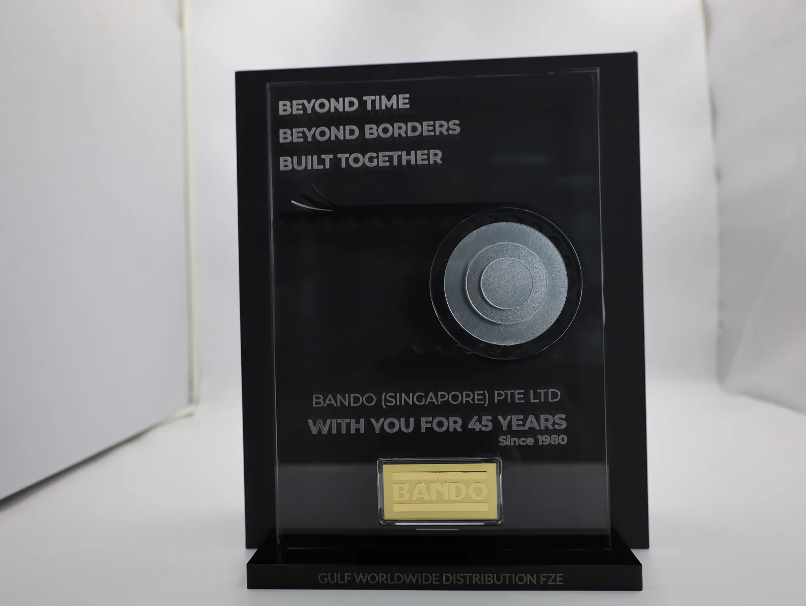 A delivered award from the front with a silver pulley, the gold BANDO bar and GULF WORLDWIDE DISTRIBUTION FZE engraved on the base