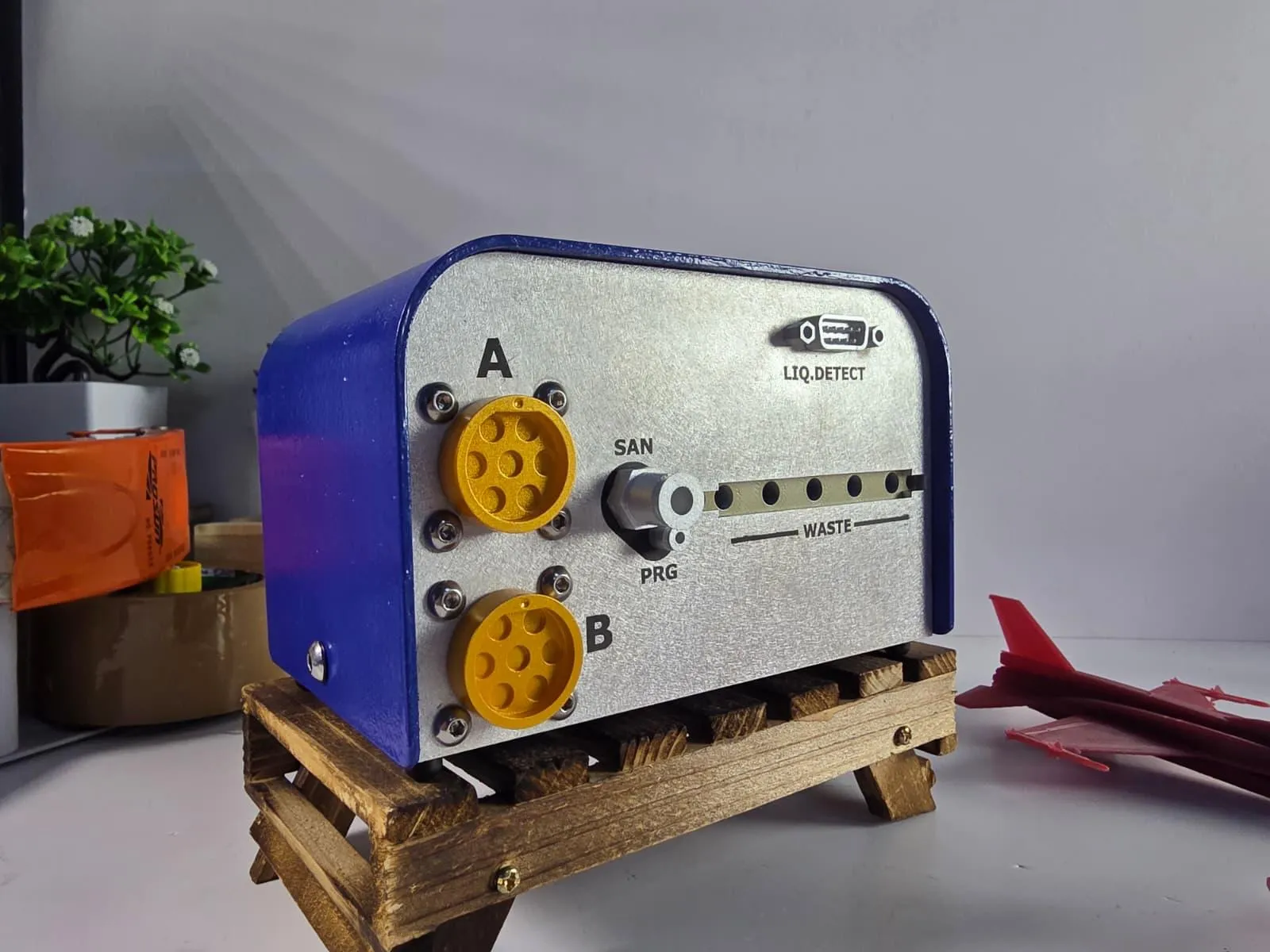 The back of the Sample Navigator replica: two yellow connectors marked A and B held by real screws, a SAN/PRG valve, a waste manifold and a LIQ.DETECT socket