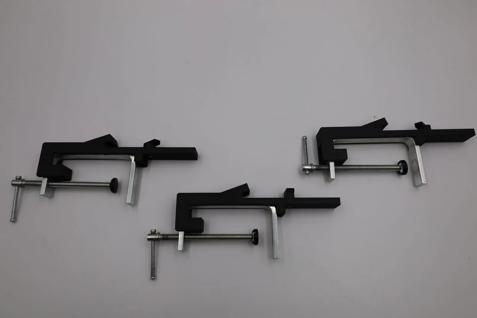 Three finished clamps laid out on a white table, each a matte black printed arm on a steel screw frame