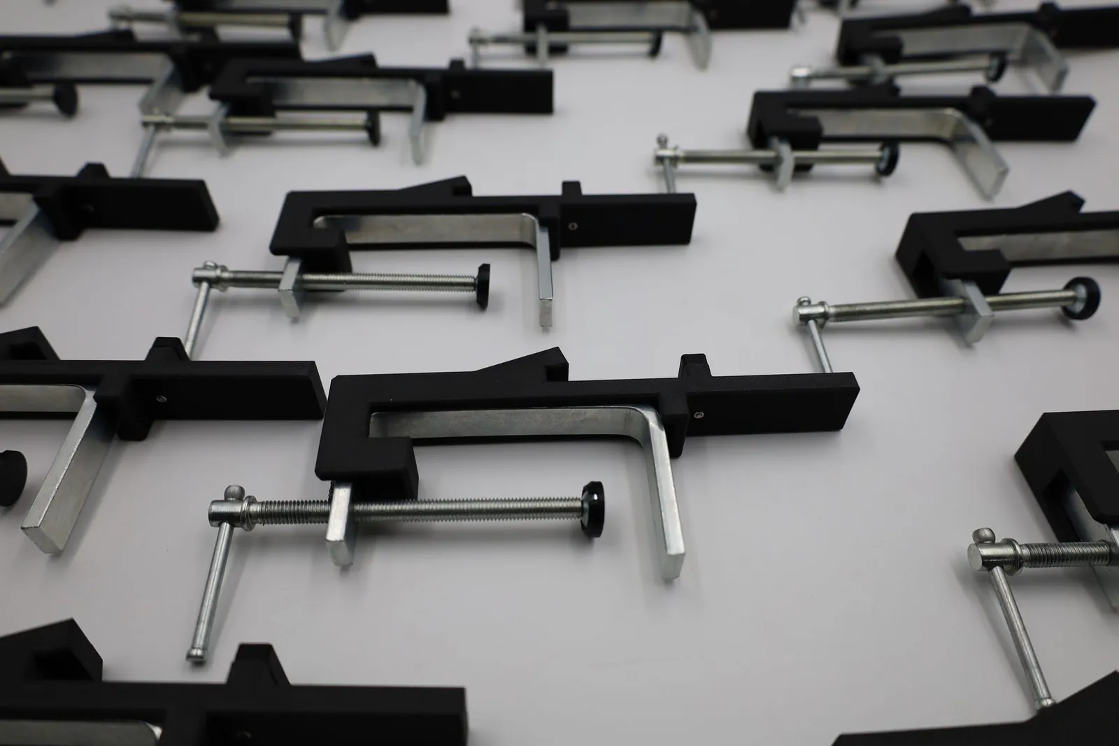 The full set of finished clamps spread across a white table, black printed arms and steel frames in rows
